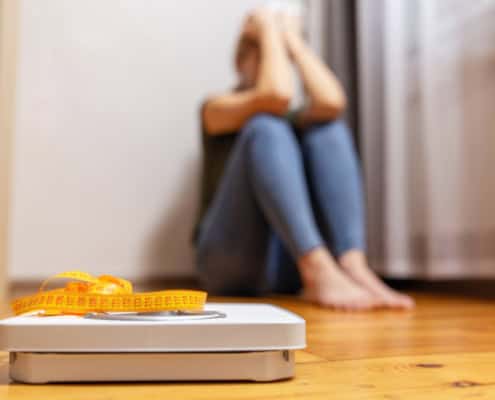 White scale and upset and sad woman with measuring tape on floor