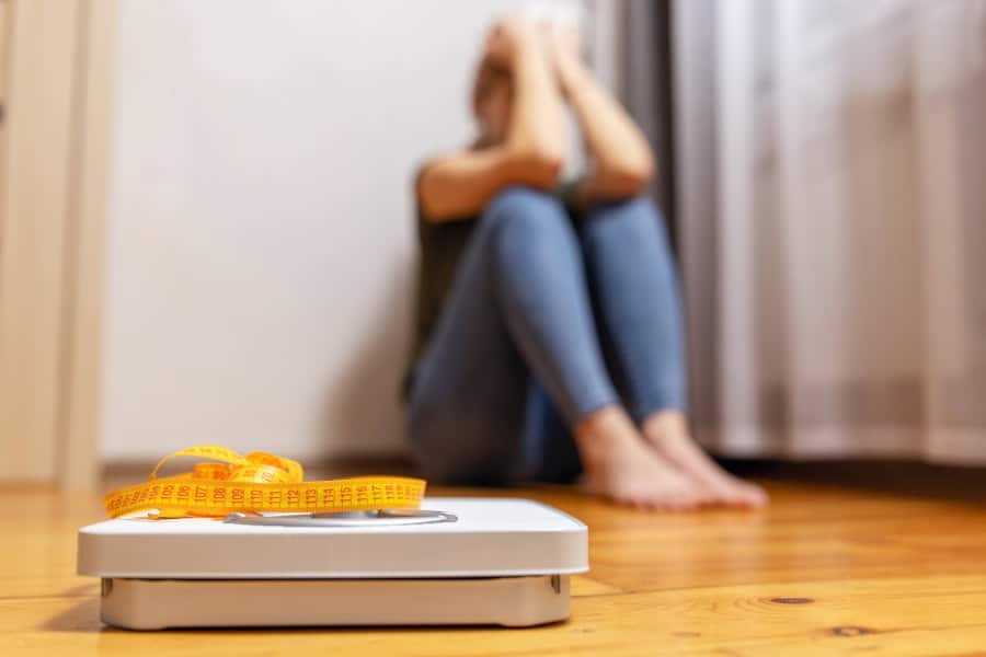 White scale and upset and sad woman with measuring tape on floor